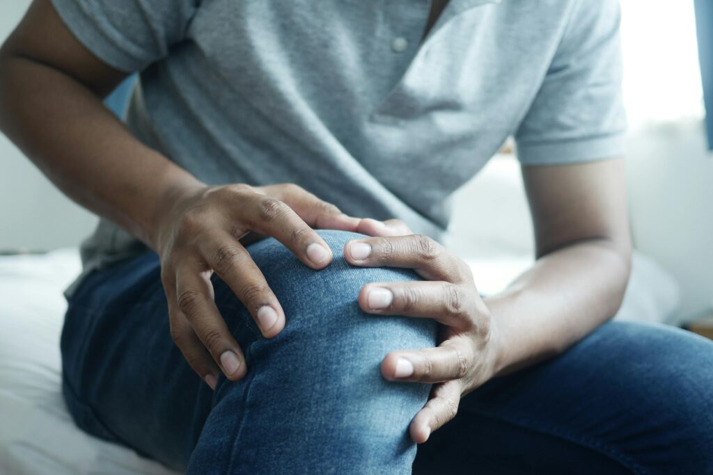 Services Close-up of a man holding his knee, capturing a moment of discomfort in a casual indoor setting.