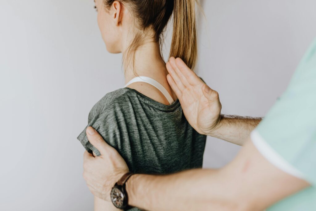 Services Back view of crop unrecognizable osteopath in uniform and wristwatch checking up back of slim female patient in casual wear on white background